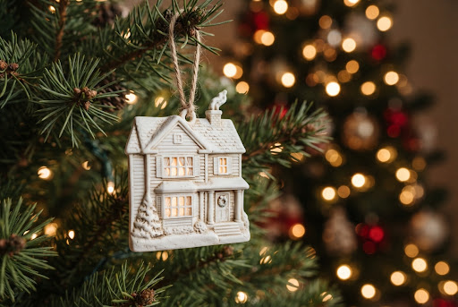 Detailed white house ornament hanging among evergreen branches and warm lights